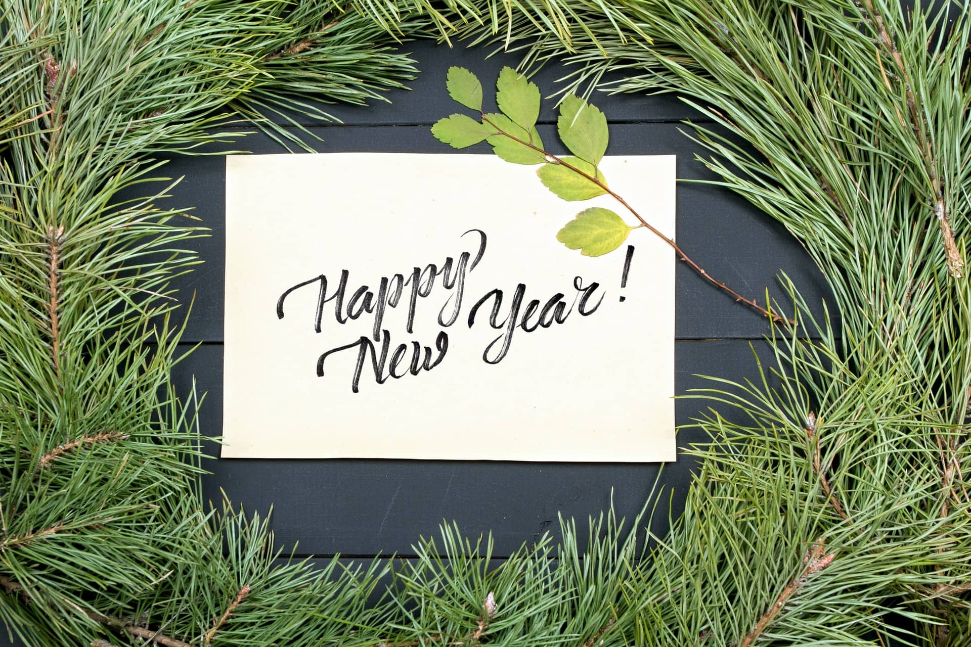 a paper with happy new year written on it surrounded by pine